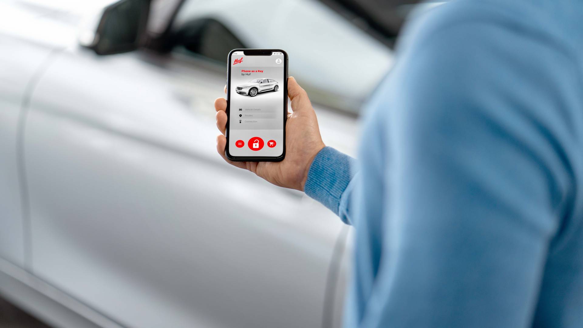 Person holding a smartphone with Phone as a Key app from Huf, gaining keyless handsfree access to a car.